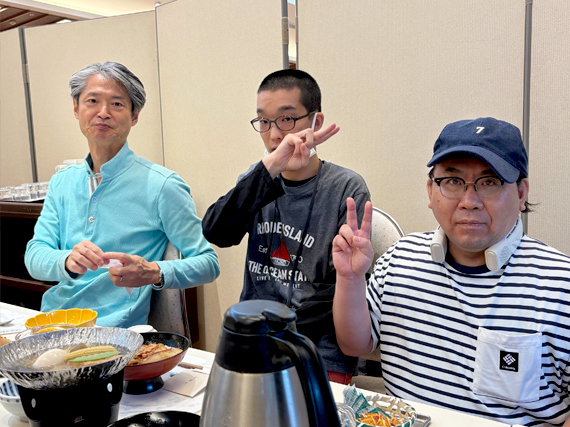 テーブルを囲み、ピースサインで食事を楽しむ3人
